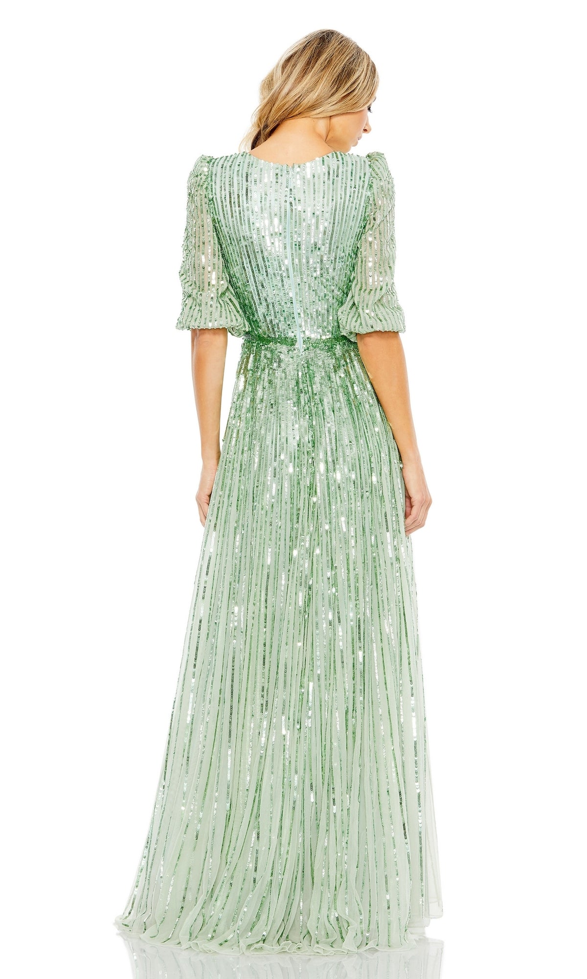 A woman stands facing away, wearing the floor-length Mac Duggal 5509: a light green formal dress with long sleeves and vertical sequin stripes.
